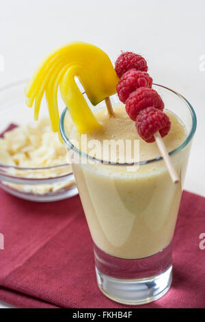 Eine gesunde Mango-Smoothie mit weißer Schokolade Späne und Himbeeren auf einem Spieß. Stockfoto