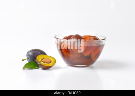 frische Pflaumen und Schüssel mit erhaltenen Pflaumen auf weißem Hintergrund Stockfoto