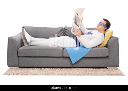 Entspannte junge Superhelden liegend auf einem grauen Sofa und liest eine Zeitung isoliert auf weißem Hintergrund Stockfoto