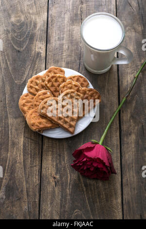 Herzförmige Waffeln, Milch und rote Rose auf dem Tisch Stockfoto