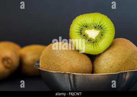 Nahaufnahme der halbierten Kiwi in metallischen Schüssel auf dunklem Hintergrund Stockfoto