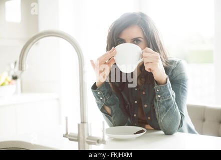 Hübsche Dame in ihren 30er Jahren Kaffeetrinken in ihrer Küche tragen blaue Jeanshemd auf ihre teabreak Stockfoto