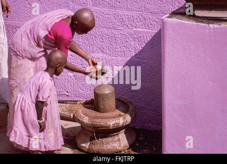 Harmonie in Farbe Pink. Rasierte Kopf Hindu-Pilger, Mutter und Tochter Gießen Sie Wasser auf Lingam am Ghat über dem Ganges. Varanasi, Indien Stockfoto