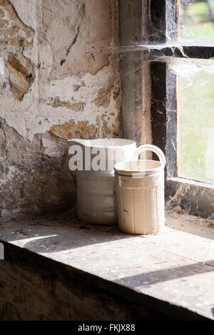 Alte Kanne und Behälter im Fenster, die im März in alten Scheunengebäuden auf der Tyneham Farm, Dorset, Großbritannien, mit Spinnweben bedeckt waren Stockfoto