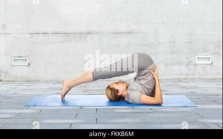 Frau macht Yoga im Pflug-Pose auf Matte im freien Stockfoto