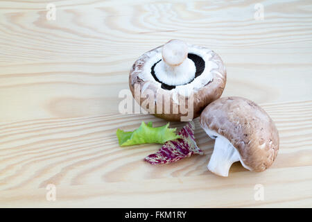 Zwei Kastanien Pilze mit einigen grünen und roten Salat auf einem Holzbrett Stockfoto