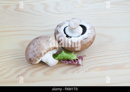 Zwei Kastanien Pilze mit einigen grünen und roten Salat auf einem Holzbrett Stockfoto