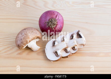 Ganzes und einen geschnittenen Kastanien Pilz mit einer roten Zwiebel auf einem Holzbrett Stockfoto