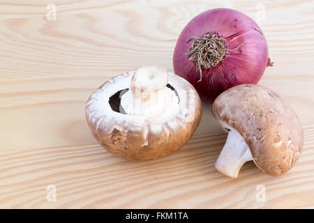 Zwei Kastanien Pilze und eine rote Zwiebel auf einem Holzbrett Stockfoto