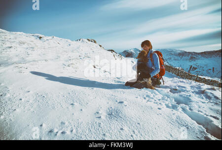Ein Wanderer, überprüfen ihre Hunde Pfoten von Schnee im Winter. VEREINIGTES KÖNIGREICH. Zusätzlichen Filmkorn und Farbe-Styling. Stockfoto