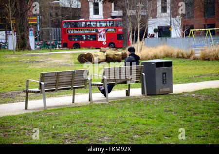 Ein Mann sitzt auf einer Parkbank mitten in Shepherds Bush gemeinsame. Stockfoto