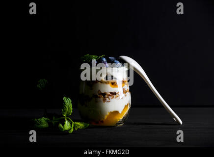 Joghurt und Hafer-Müsli mit Marmelade, Blaubeeren und Minze Blätter in Glas auf schwarzem Hintergrund, selektiven Fokus Stockfoto