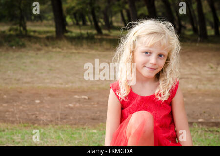 entzückende kleine Mädchen im roten Kleid sitzt Stockfoto