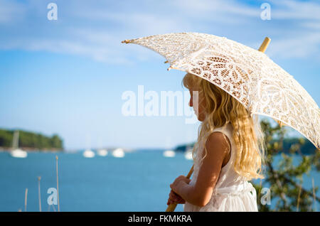 kleines Mädchen im weißen Kleid posiert mit weißen Sonnenschirm Stockfoto