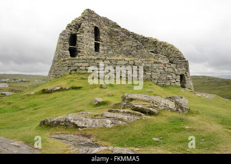 2.000 Jahre alten Dun Carloway Broch an einem bewölkten Tag mit ein paar Häuser von Dun Carloway Dorf im Hintergrund auf der linken Seite. Stockfoto