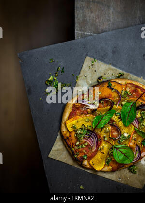 Hausgemachte vegane Pizza auf Schiefer Brett auf Holztisch. Ansicht von oben. Stockfoto