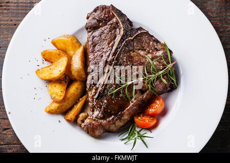 Gegrilltes t-Bone Steak mit gebratene Kartoffelspalten auf weißen Teller auf hölzernen Hintergrund hautnah Stockfoto