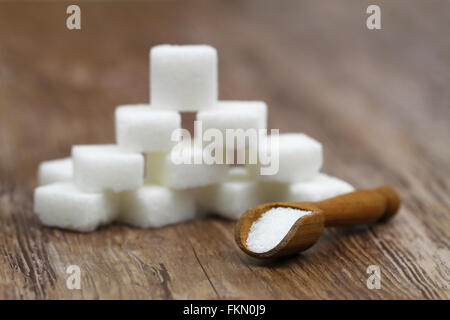 Weißer Zucker auf hölzerne Schaufel und weißen Zuckerwürfel gestapelt im Hintergrund Stockfoto
