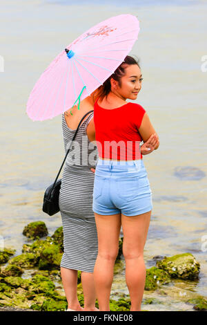 Zwei asiatische Mädchen stehen am Rand Wassers von Tampa Bay hält einen Papier-Sonnenschirm