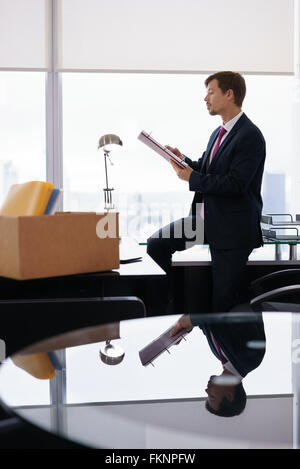 Geschäftsmann vor kurzem eingestellt für corporate Job zieht in sein neues Amt. Er nimmt Sie einen Ordner aus einer Box und liest Dokumente nea Stockfoto