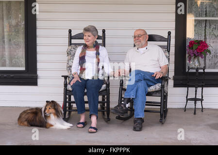 Einem älteren Ehepaar in den achtziger Jahren beobachten das rege Treiben von ihrer Veranda mit ihrem Sheltie Hund an ihrer Seite. Stockfoto