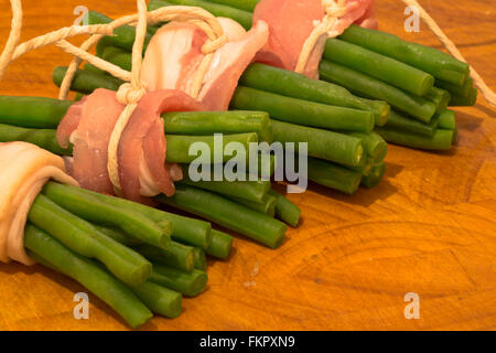 Frisch zubereitete Trauben von Baby grüne Bohnen mit Streifen von geräuchertem Speck umwickelt und mit Schnur, bereit für den Backofen gebunden. Stockfoto