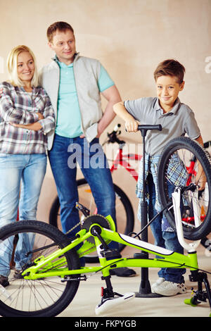 Süsser Boy Reparatur sein Fahrrad selbst mit seinen Eltern, die hinter Stockfoto