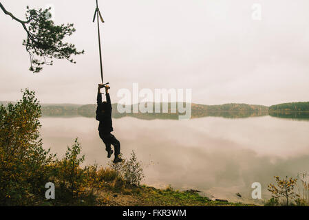 Mann hängen am Seil schwingen am abgelegenen See Stockfoto