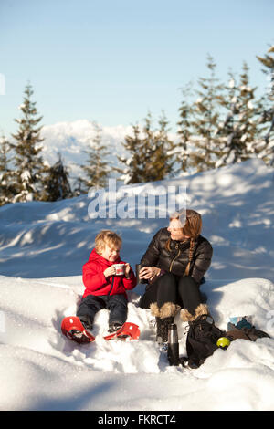 Kaukasische Mutter und Sohn trinken heißen Kakao im Schnee Stockfoto