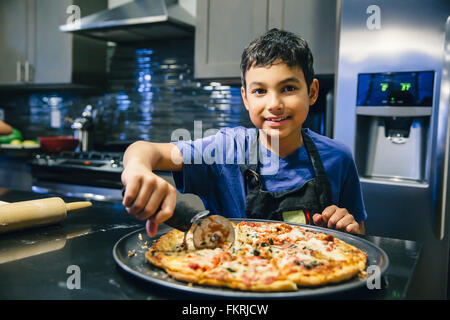 Gemischte Rassen junge schneiden Pizza in Küche Stockfoto