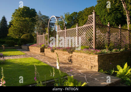 Pfad, blühende Pflanzen, Rasen, Wand, Rankgitter Bogen und Bildschirm - schöne sonnige, gestaltete, landschaftlich, Burley in Wharfedale, Yorkshire, England Garten. Stockfoto