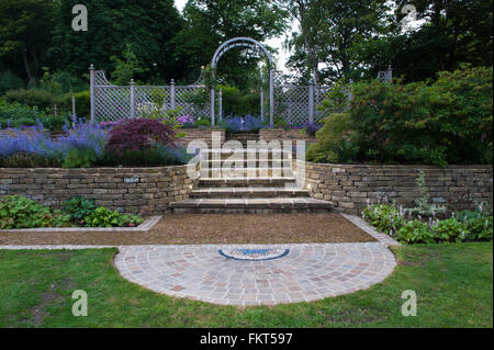 Mosaik-Kunst, Pflasterarbeiten, Blütenpflanzen, Schritte und Rankgitter Bogen in der Dämmerung - gestaltete, gepflegten Garten, Burley in Wharfedale, Yorkshire, England. Stockfoto