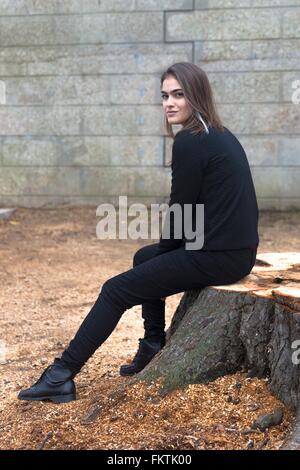 Junge Frau sitzt auf Baumstumpf Stockfoto