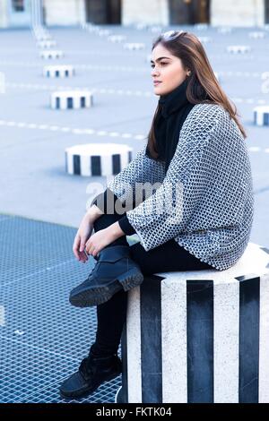 Junge Frau sitzt auf gestreiften konkrete Hocker, Le Palais Royal, Paris, Frankreich Stockfoto