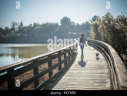 Voller Länge Vorderansicht junge Frau erhöhten Holzsteg Wandern Hund Stockfoto