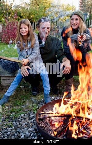 Mädchen mit Mutter und Vater sitzen im Garten mit Feuerstelle Stockfoto