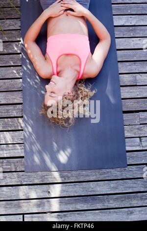 Junge Frau, die auf Yoga-Matte, hoher Winkel liegen