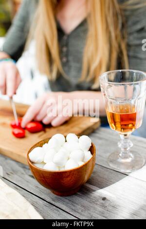 Frau hacken Tomaten mit Getränk im Glas im Vordergrund Stockfoto