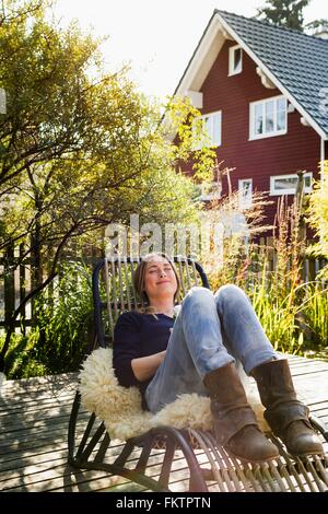 Mitte Erwachsene Frau entspannend auf Liegestuhl auf Holzterrassen Stockfoto