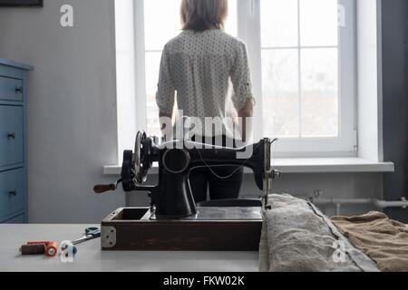 Rückansicht des Frau Blick aus Fenster und Vintage Nähmaschine Stockfoto