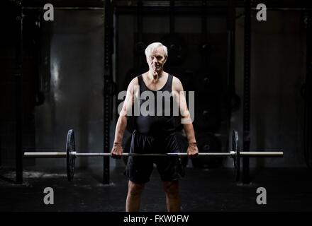 Senior woman Gewichtheben Langhantel in dunklen Turnhalle Stockfoto