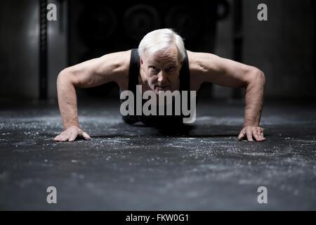 Oberfläche Sicht auf ältere Mann tut Push ups in dunklen Turnhalle Stockfoto