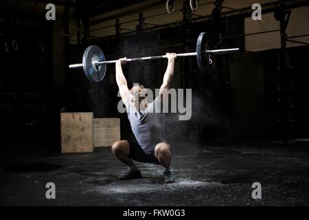 Junger Mann Gewichtheben Langhantel in dunklen Turnhalle Stockfoto