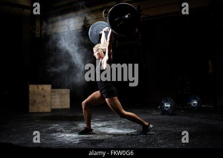 Seitenansicht der jungen Frau Gewichtheben Langhantel in dunklen Turnhalle Stockfoto