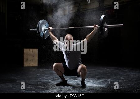 Junger Mann Gewichtheben Langhantel in dunklen Turnhalle Stockfoto