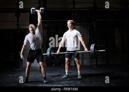 Zwei junge Männer Gewichtheben mit Kurzhantel und Langhantel in dunklen Turnhalle Stockfoto