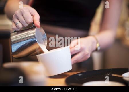 Beschnitten, Schuss Kellnerin gießt Milch in die Kaffeetasse im café Stockfoto