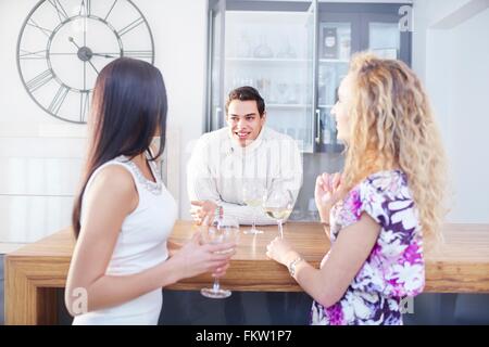 Drei junge Erwachsene Freunde plaudern und trinken Wein in Küche Stockfoto