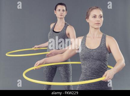 Junge Frauen, die sich darin üben, mit Hula-Hoop, grauer Hintergrund Stockfoto