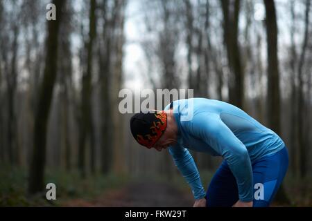 Läufer mit Stricken Hut und Elasthan Biegung nach vorne Hände auf Knien erschöpft Stockfoto